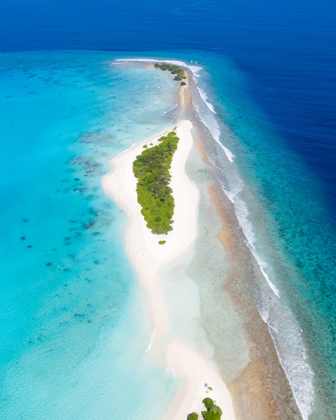 A narrow sandbank with a patch of green, surrounded by turquoise lagoon